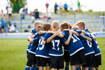 Boys football team forming huddle. Happy kids in a sports team on grass pitch. Summer school soccer tournament. Children playing sports outdoor