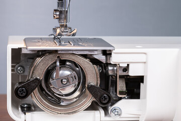Foot and needle with vertical shuttle mechanism of the sewing machine. Sewing equipment. Close-up of sewing machine elements.