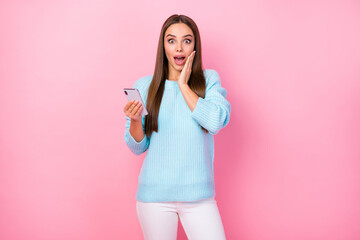 Photo of pretty shocked lady hand on cheek hold telephone check followers many likes comments wear knitted blue sweater white trousers isolated pastel pink color background