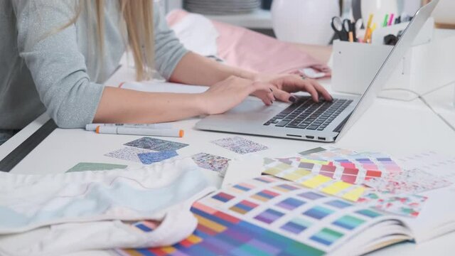 Gentle female arms at table with pens coloured layouts and other stuff using touchpad on modern laptop and light and good office room