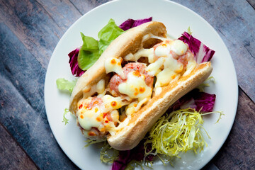 A meatball sandwich served in a hot dog bun with melted cheese on a bed of mixed salad