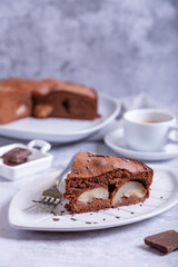Piece of chocolate pie with pear. In the background is a pie, a cup of coffee and pieces of chocolate. Close-up.