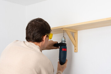 A man hangs a shelf in an apartment on a white wall, a worker tightens screws on a shelf corner...