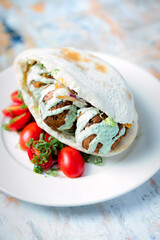 Pitta bread meatball sandwich served with yogurt sauce and cherry tomatoes on the side
