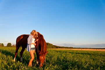 Young girl walking with a horse in the field