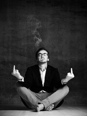 Brutal man in jacket, jeans, glasses and barefoot sitting on floor, smoking cigarette and...