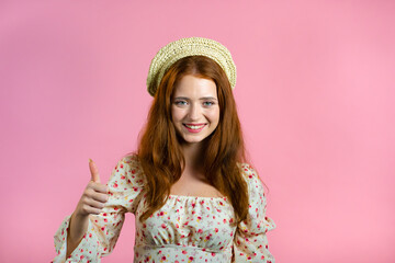 Lady with long hair shows thumbs up, Like gesture. Happy woman on pink background. Winner. Success. Positive girl smiles to camera. Body language.