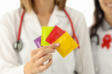 Doctor in white suit hold in hand four condom of different colors. Nurse with red lisbian symbol on her chest.