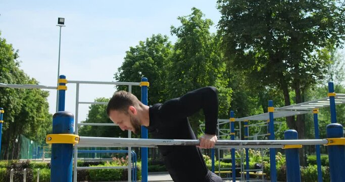 Man in sportswear doing triceps dip exercise on parallel bars at park