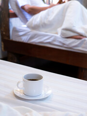 White Coffee Mug Rests on The White Mattress behind The Man Sitting
