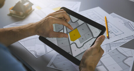man searching building plot to buy on cadastral plan for house construction on digital tablet © ronstik