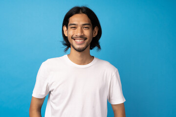 A handsome young Asian man wearing a white T-shirt, smiling happily and standing with his arms crossed in a studio with a light blue background.