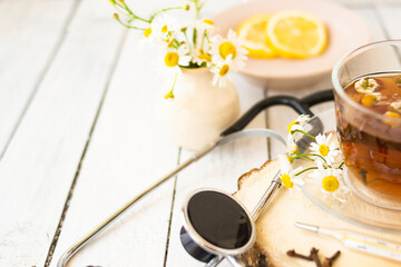 Obraz na płótnie Canvas Decoction of chamomile, dried flower in flower tea and a phonendoscope, sliced lemon on a white wooden background. Health concept, prostate treatment, doctor prescribing treatment