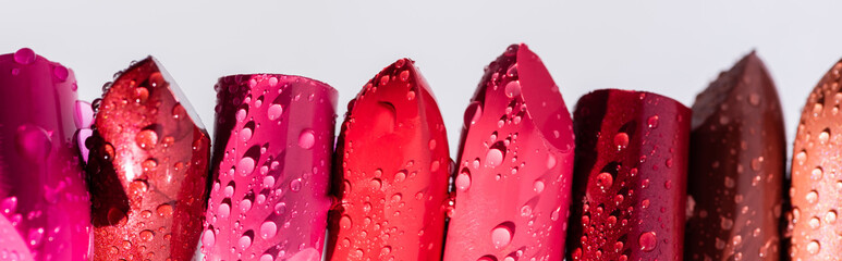 Close up view of wet lipsticks in row isolated on white, panoramic shot