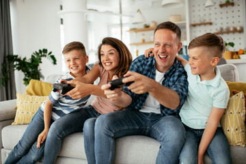 Husband and wife playing video games with joysticks in living room. Loving couple are playing video games with kids at home
