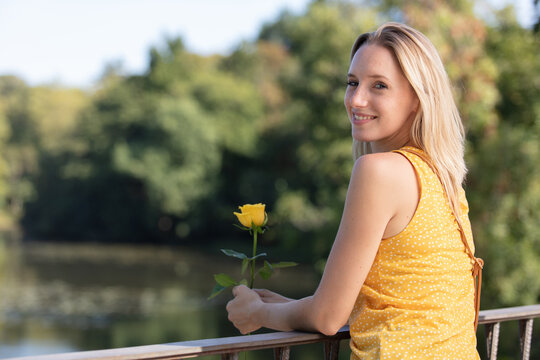 Young Woman Holding Yellow Rose Standing Overlooking A River