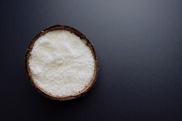 Coconut flakes in a bowl of coconut on a gray background.