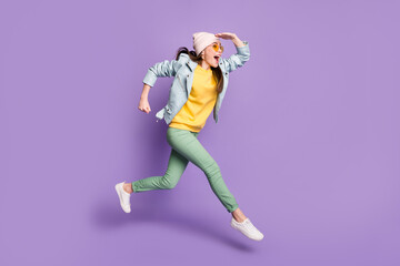 Full size profile side photo of excited cheerful girl see discover incredible discount jump run fast wear headwear green pants trousers leather jacket isolated purple color background