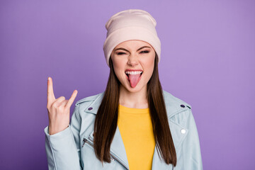 Closeup photo of good mood pretty lady sticking tongue out mouth teasing behavior crazy rocker showing horns wear casual hat blue modern jacket isolated purple color background