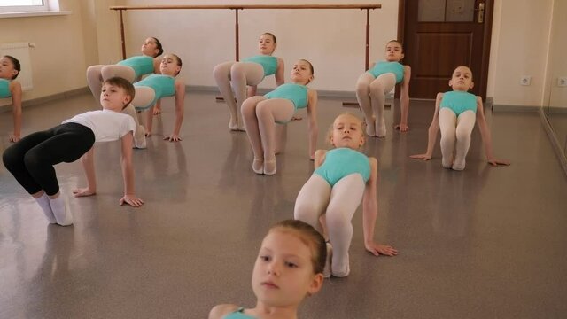 Group of ballet girls doing stretching exercises before dance lessons. Ballerinas training at hall.