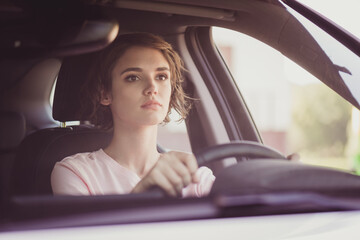 Photo of charming cute lady serious indifferent face hands hold steering wheel drive car carefully self-assured look road ride through dangerous unfamiliar turn wear white shirt indoors