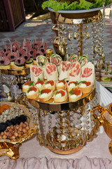 Set a buffet table. A golden dish containing various sandwiches and canapes. A sandwich with caviar, sausage, drinks are all placed on a beautiful table.