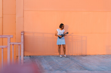 Young beautiful woman playing ukulele and having fun at the background of a coral wall