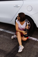 Young beautiful woman sitting and having fun with ukulele near car at the parking