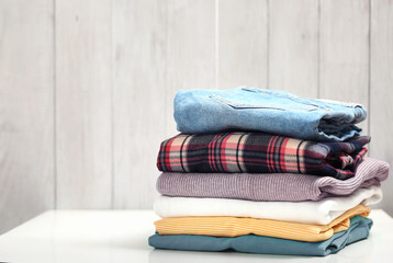 Stack of clothing on white table wooden plank background.Folded clothes pile empty copy space.