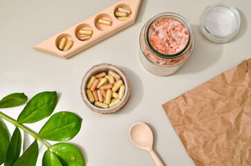 Herb in capsules in wooden bowl on pastel beige background. Beauty products for face and body skin care