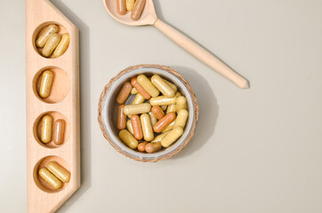 Herb in capsules in wooden bowl on pastel beige background. Beauty products for face and body skin care