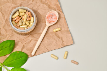 Herb in capsules in wooden bowl on pastel beige background. Beauty products for face and body skin care