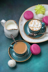 Blue coffee cups with cream and marshmallows, with coconut candies on a blue background