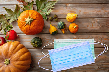 Covid 19 protective mask and thanksgiving pumpkins against wooden background, top view