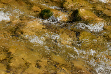 The seething water of the river runs over large and small stones. The water in the river is clear, it runs quickly and the entire bottom is visible.