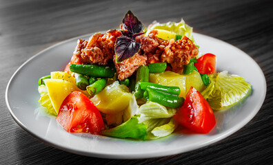Salad nicoise. Tuna, with green beans, tomatoes, potatoes and a vinaigrette mustard dressing in white plate on black wooden table background