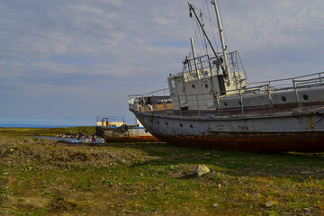 Old rusty abandoned boats, white ships lie on green grassy shore in the light of setting sun. Lake Baikal, Bolshoe Goloustnoe
