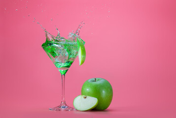 Appletini cocktail splashes and green apple on pink color background with space for text