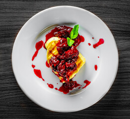 Halloumi cheese frying with cherry in plate on black wooden table