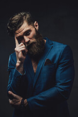 Brutal and handsome man with beard and stylish haircut posing with finger to his head in dark background.
