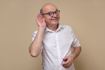 Senior bald male adult in glasses listening carefully, spying, being curious. Studio shot