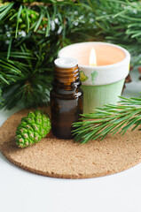 Obraz na płótnie Canvas Small glass bottle with essential pine oil, pine branches, green cone and burning candle. Aromatherapy, spa and herbal medicine ingredients. Copy space.
