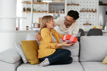 Boyfriend surprising his girlfriend with a gift. Young man giving gift box to his wife.