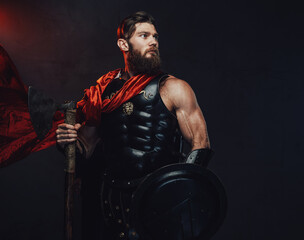 Atmospheric and dark room with spotlight and roman guardian with muscular build and beard holding axe and shield whihc posing in it.