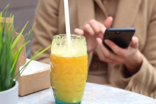 Modern an creative Woman watching mobile phone and drinking orange juice in autdoor cafe. Autumn. Spring. 