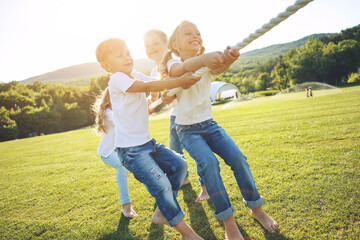 Fototapeta premium Children play tug of war in the park. A group of cute children playing actively together in nature. Cute kids outdoors. High quality photo.