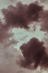 portrait image of a group of storm clouds, shaded in brown, surrounding a cloudy sky.