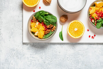Bright fruit salad and ingredients on the table top view. Salad of oranges, pomegranates, spinach and nuts in a bowl on a white background. Healthy diet food, vegetarian food. Copy space