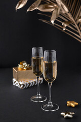 Two glasses of champagne over black background and golden Christmas decoration. Holiday decorations on dark table.