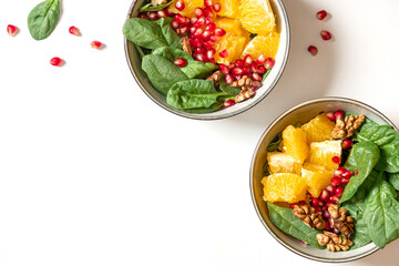Bright fruit salad top view. Salad of oranges, pomegranate, spinach and nuts in a bowl on a white background. Free space for text. Healthy diet food, vegetarian food. Copy space.